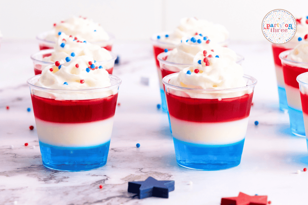 Side view of festive 4th of July Jello shots arranged on a marble surface with red, white, and blue star decorations around them.