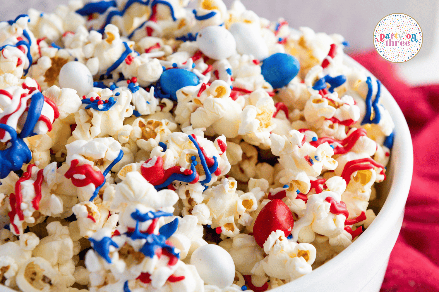 Close-up of patriotic popcorn with candy drizzle, sprinkles, and M&Ms in red, white, and blue.