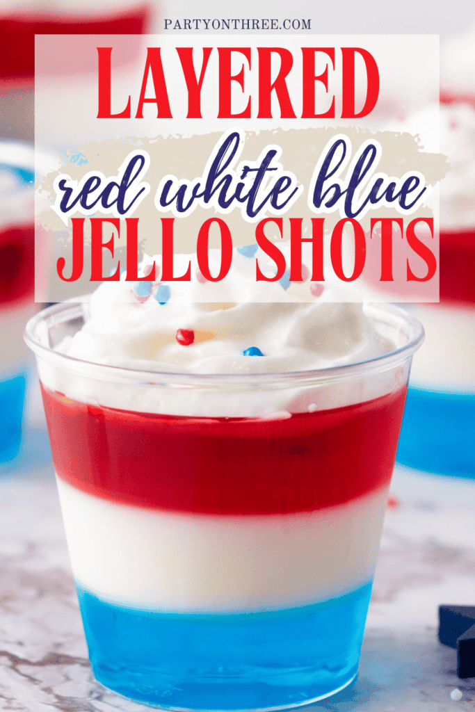 Close-up of a red, white, and blue Jello shot in a clear cup with whipped cream and sprinkles, with text reading “Layered red white blue Jello Shots – partyonthree.com.”