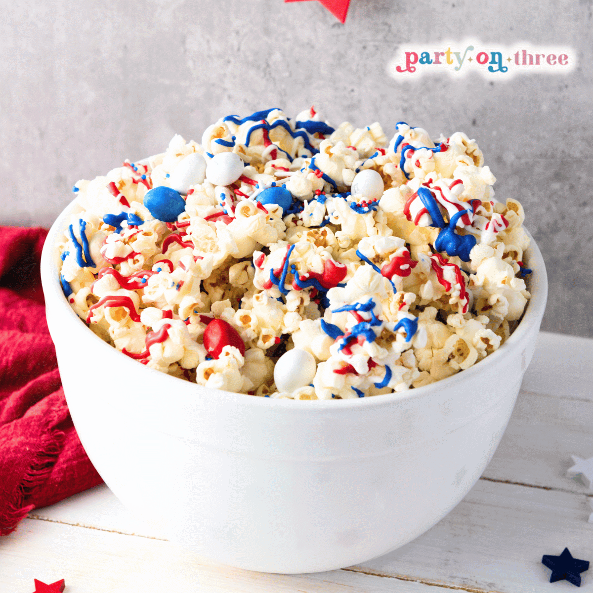 Bowl of patriotic popcorn with red, white, and blue candy drizzle and M&Ms, perfect for a Fourth of July snack.