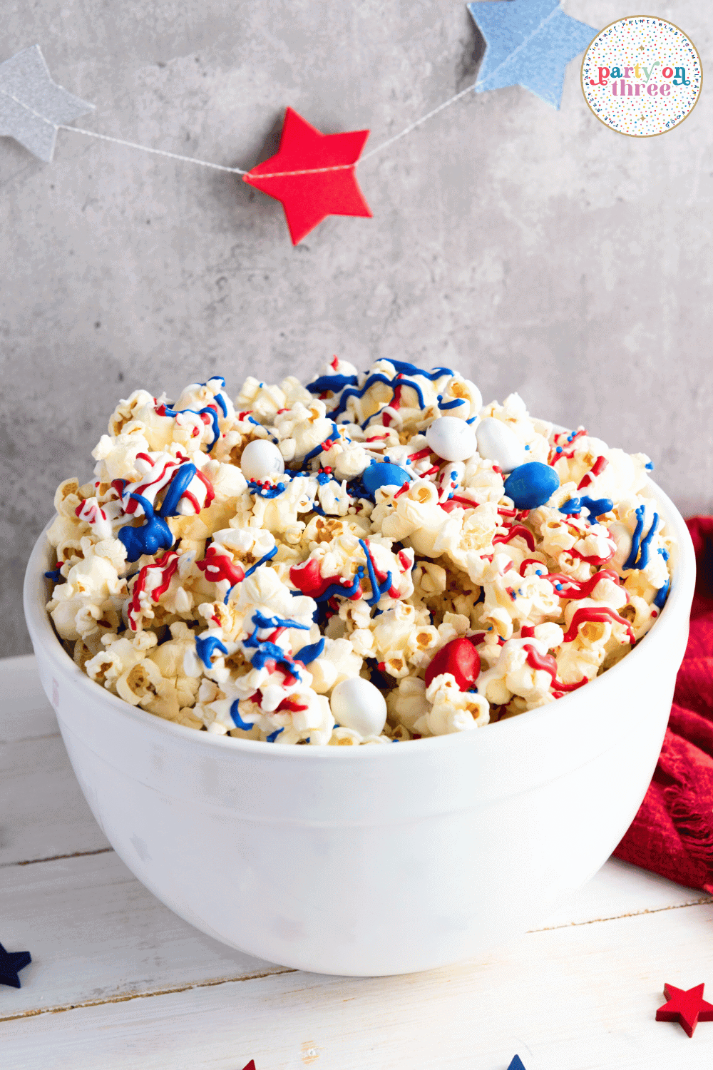 White bowl filled with patriotic popcorn and a red star garland in the background for a festive Fourth of July party.