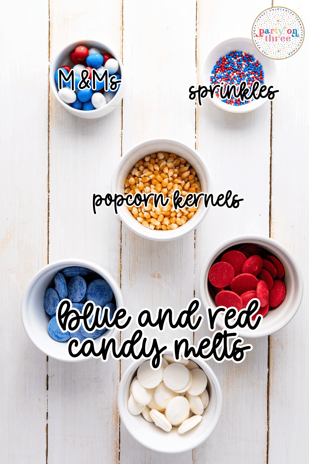 Small bowls of ingredients for patriotic popcorn including M&Ms, sprinkles, popcorn kernels, and red, white, and blue candy melts.
