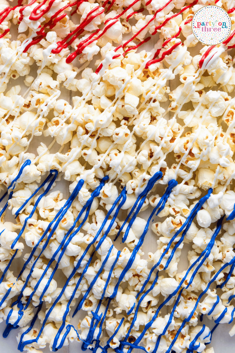 Popcorn drizzled with melted red, white, and blue candy melts in clean stripes on parchment paper.