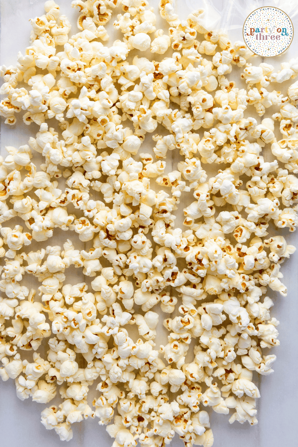 Freshly popped plain popcorn spread out on parchment paper before adding candy drizzle and toppings.

