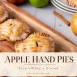 Glazed apple hand pies on a wooden tray with fresh apples and cinnamon sticks in the background