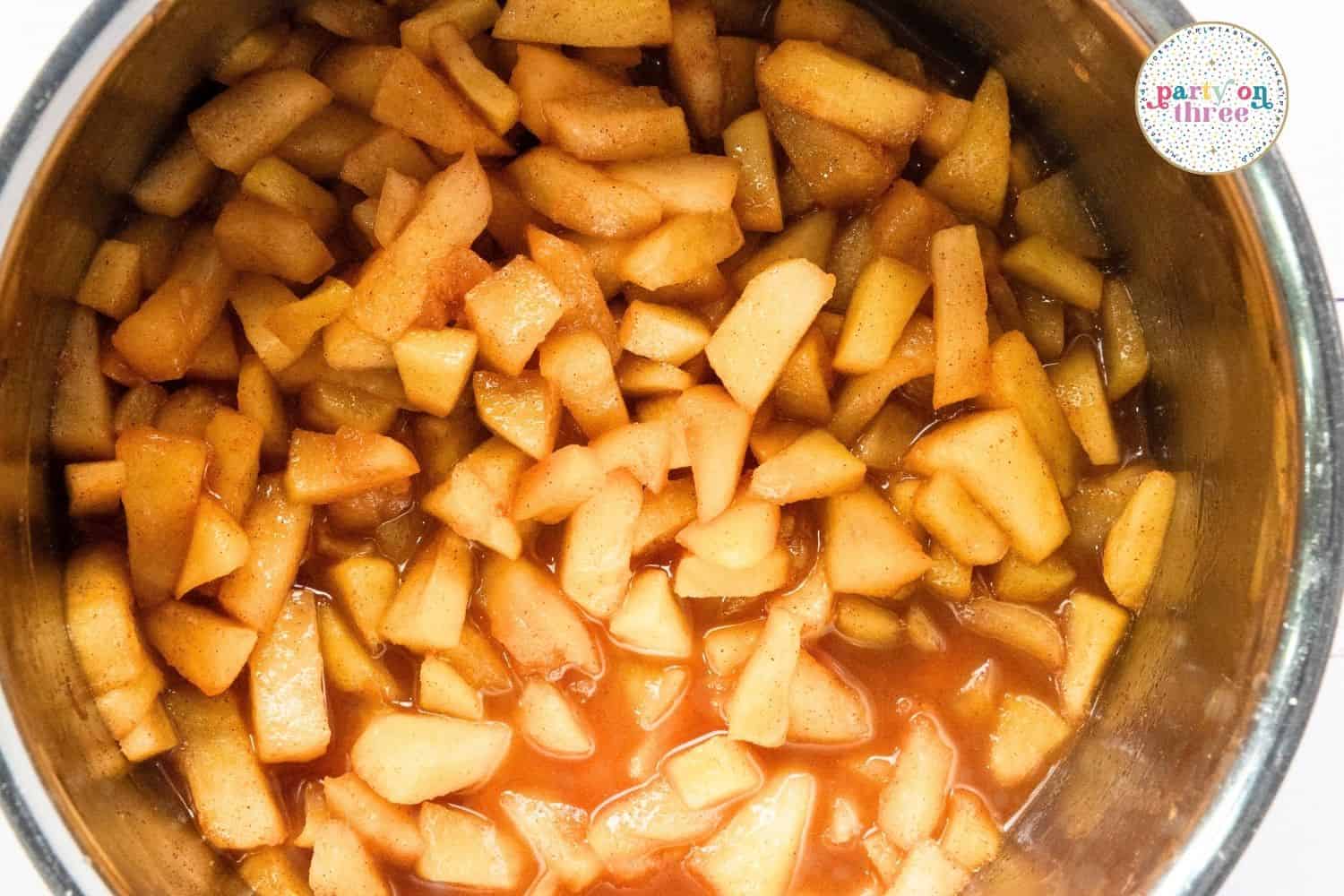 Diced apples simmering in a pot with cinnamon and syrupy liquid until glossy and just softened