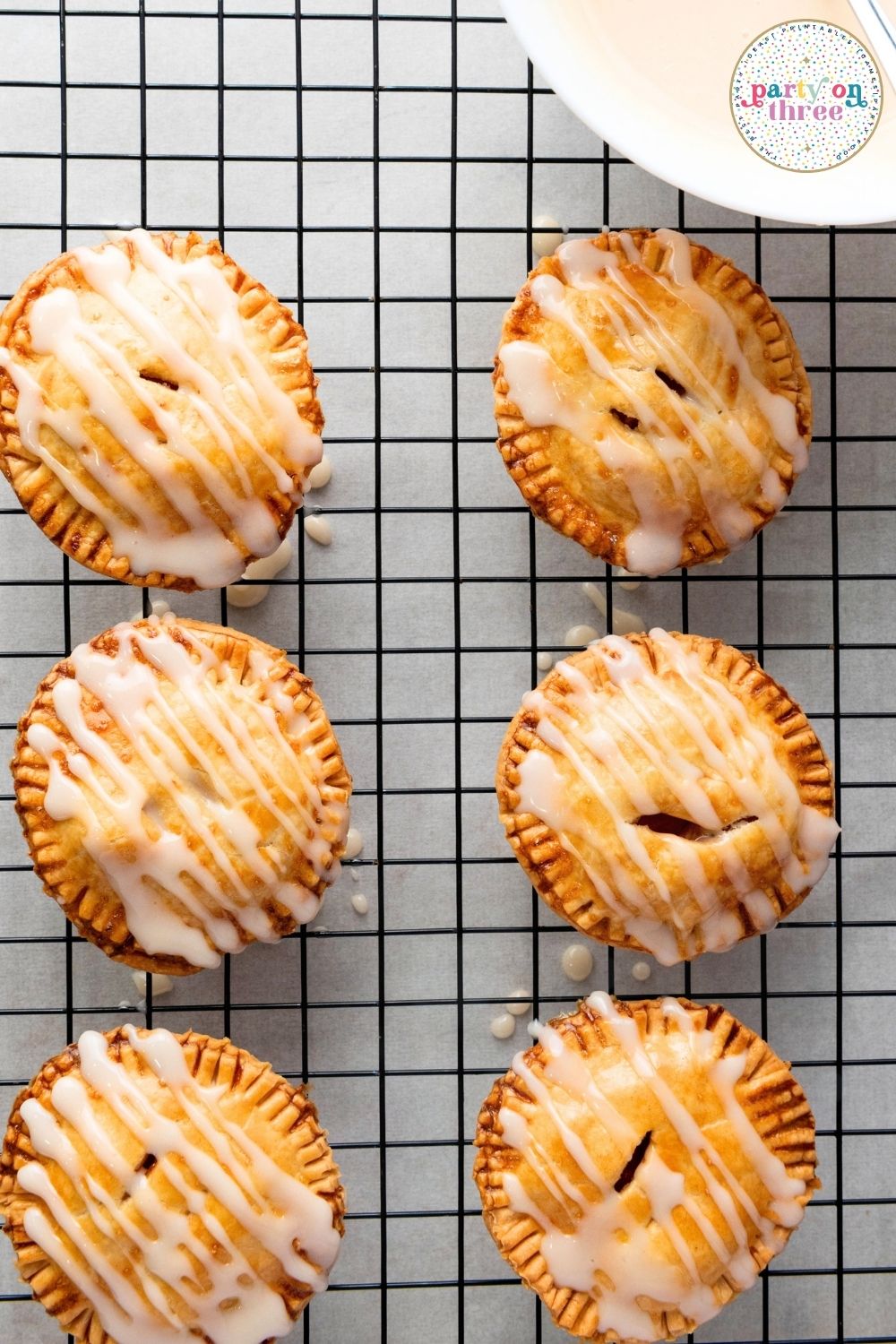 Baked apple hand pies drizzled with glaze cooling on a wire rack