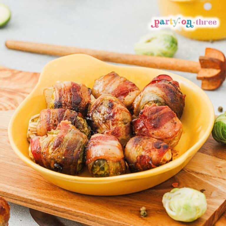 Close-up of Maple Bacon Wrapped Brussels Sprouts in a yellow dish on a wooden board