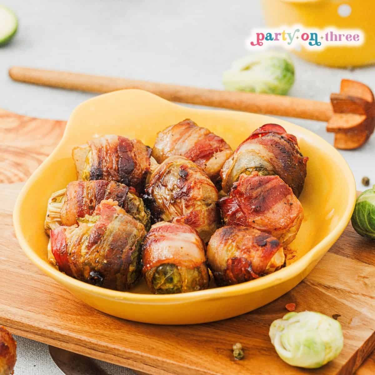 Close-up of Maple Bacon Wrapped Brussels Sprouts in a yellow dish on a wooden board