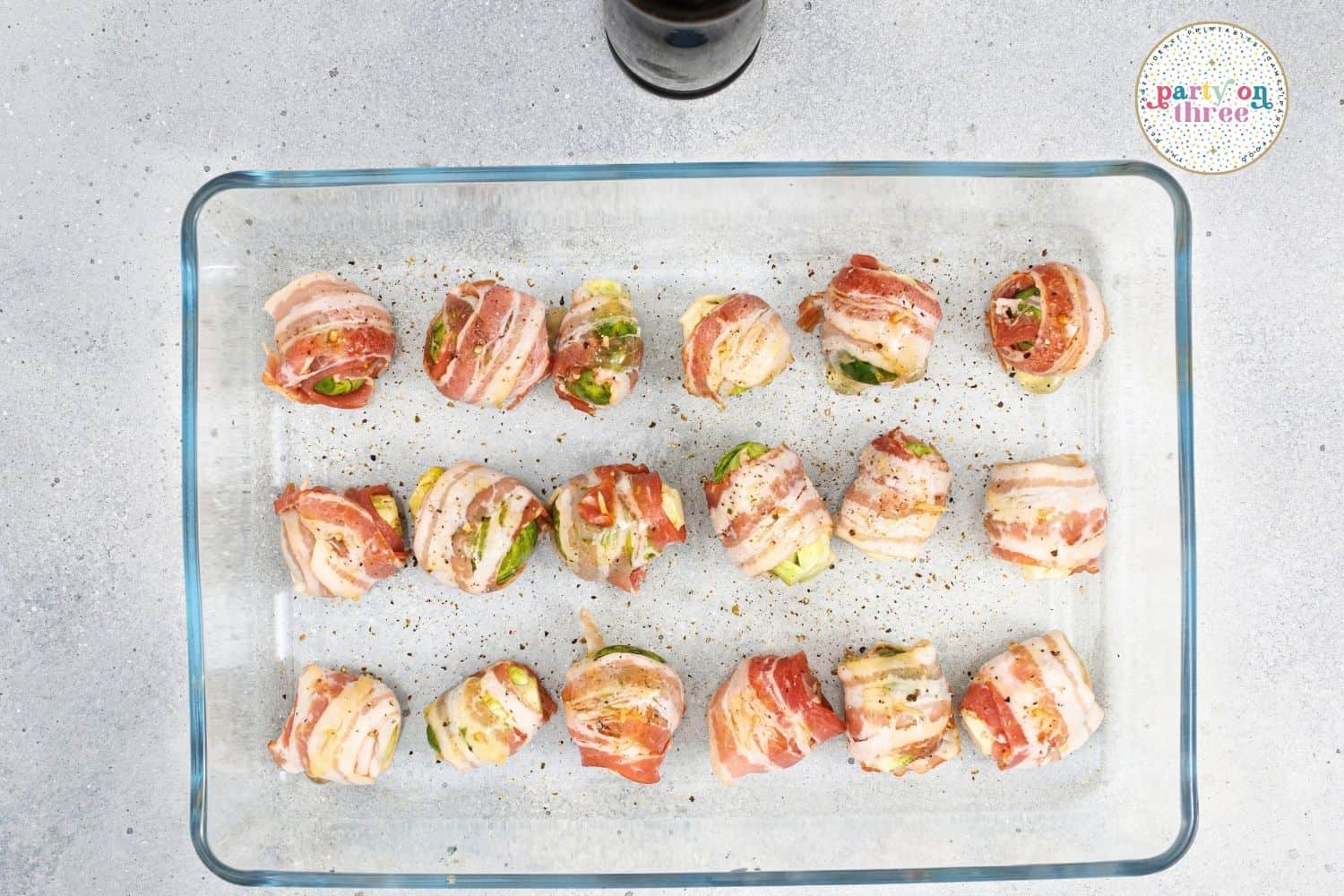 Rows of raw bacon-wrapped brussels sprouts arranged in a glass baking dish before roasting