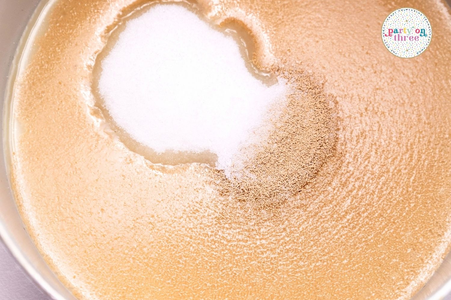 Sugar and yeast being added to a bowl of liquid for pumpkin cinnamon roll dough