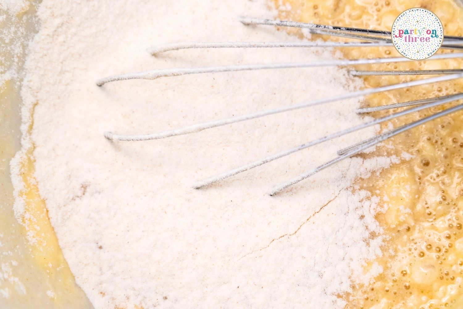 Whisking flour into a wet batter for pumpkin cinnamon roll dough in a mixing bowl