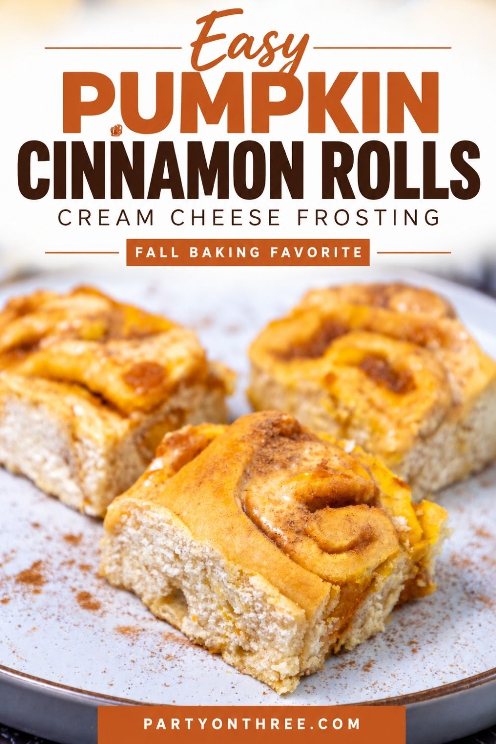 Three pumpkin cinnamon rolls on a speckled plate dusted with cinnamon