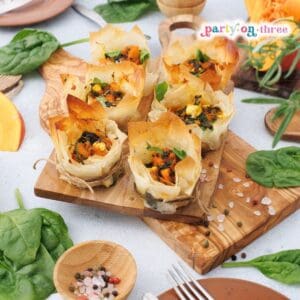 Baked pumpkin feta phyllo cups on a wooden board surrounded by spinach and pumpkin slices