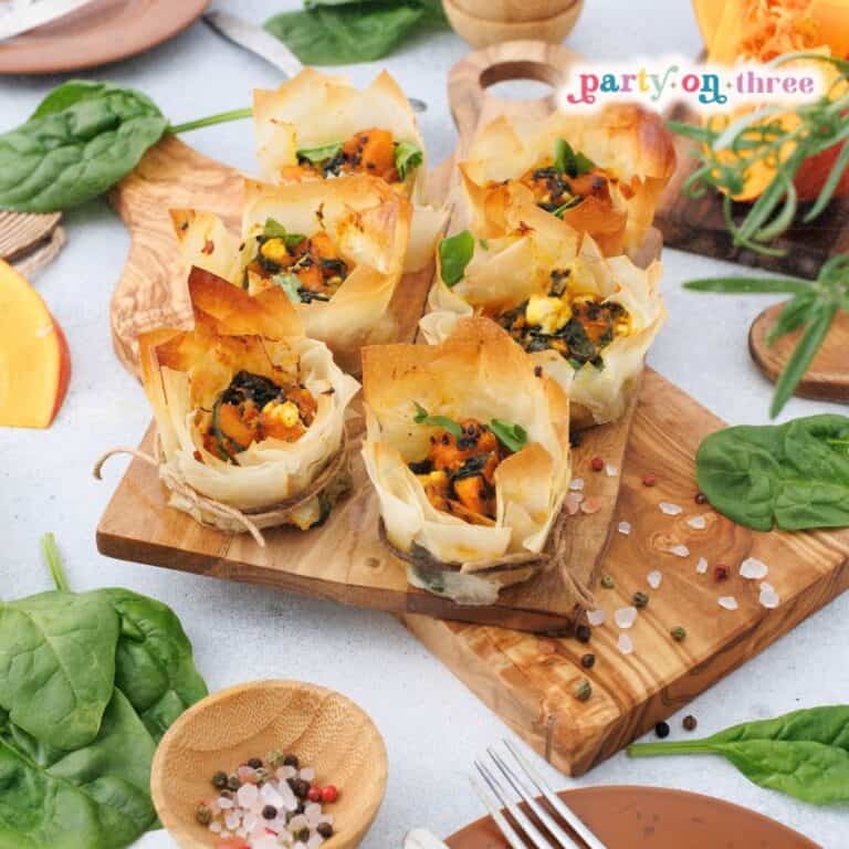 Baked pumpkin feta phyllo cups on a wooden board surrounded by spinach and pumpkin slices