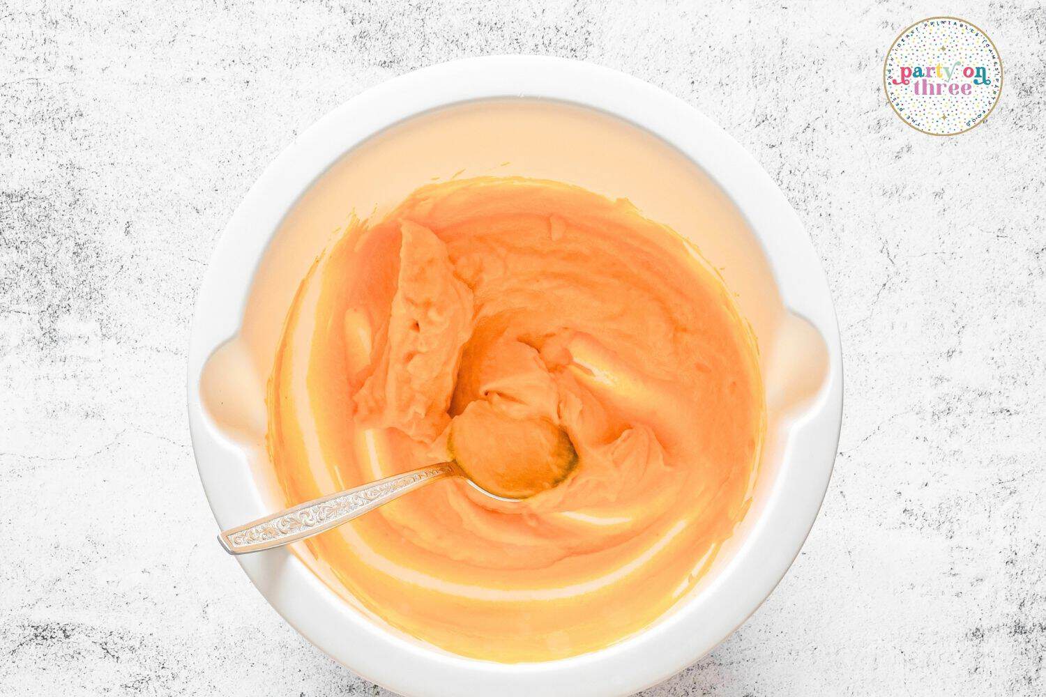 Whisked pumpkin puree, cream, egg and vanilla mixture in a white bowl with a spoon