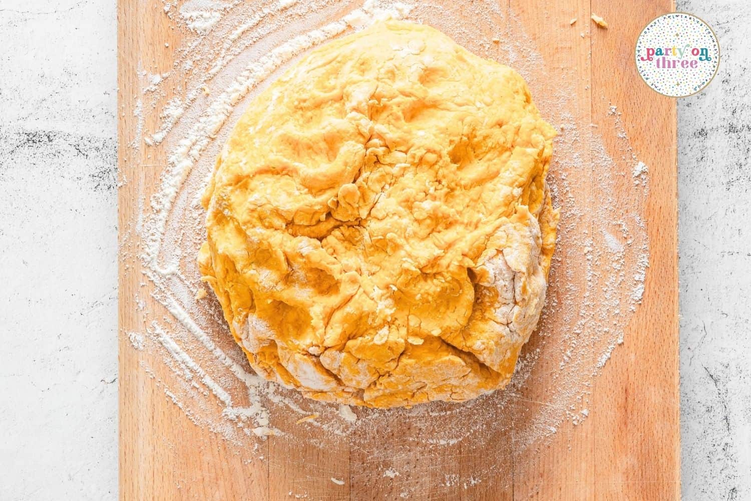 Kneaded pumpkin scone dough shaped into a round on a floured wooden board