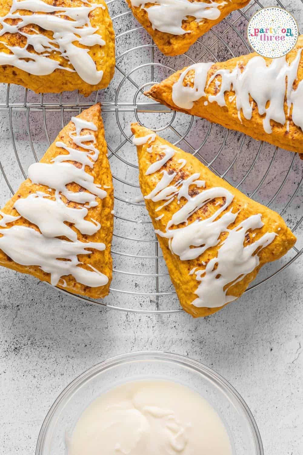 Whisked vanilla glaze in a glass bowl with glazed pumpkin scones cooling on a wire rack nearby