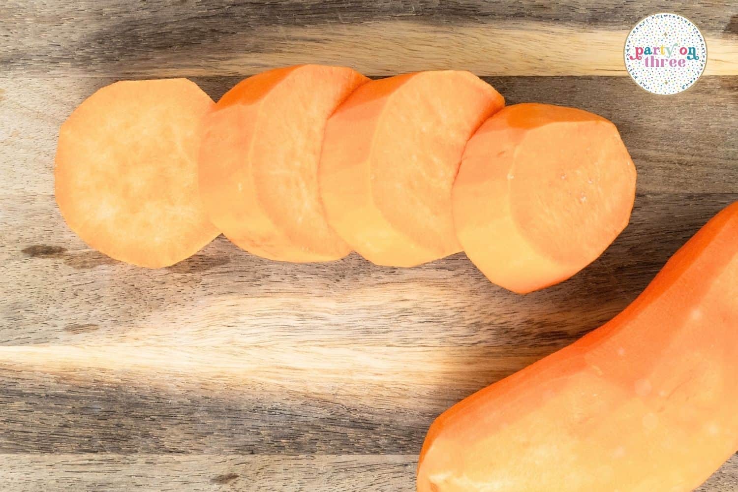 Peeled sweet potato sliced into four even rounds on a wooden cutting board