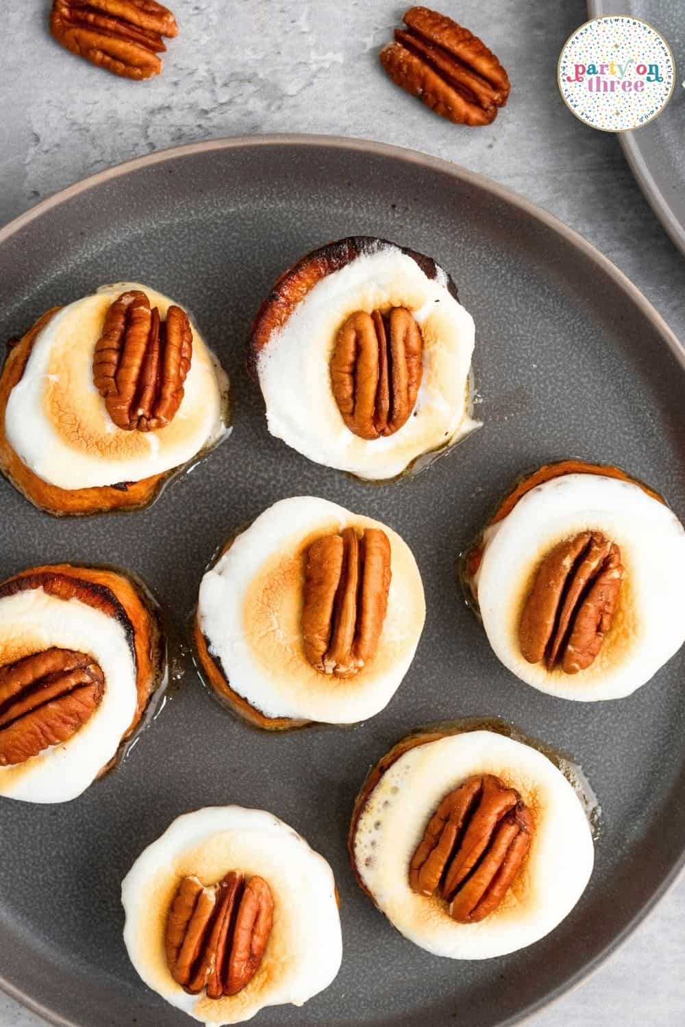 Toasted marshmallow halves topped with pecan halves resting on baked sweet potato rounds on a plate