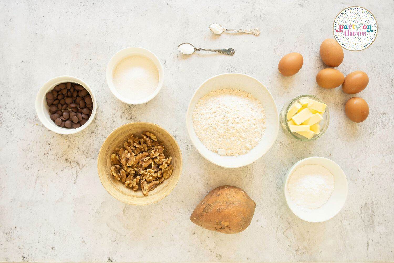 Ingredients for sweet potato bread laid out: sweet potato, flour, eggs, butter, walnuts, chocolate chips