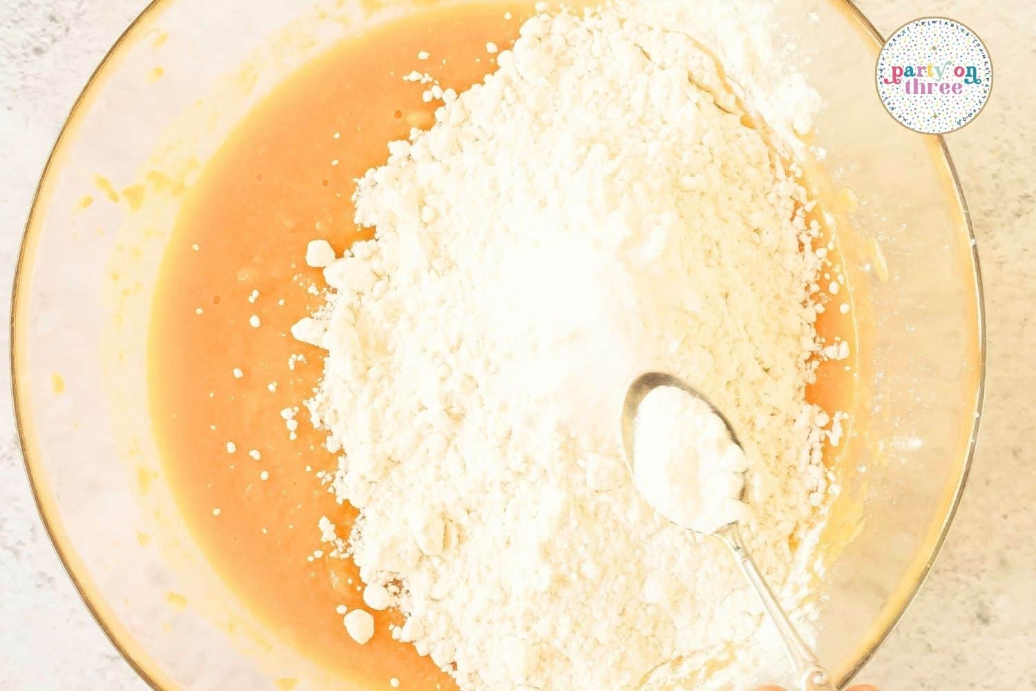 Flour being added to a bowl of wet sweet potato batter with a spoon