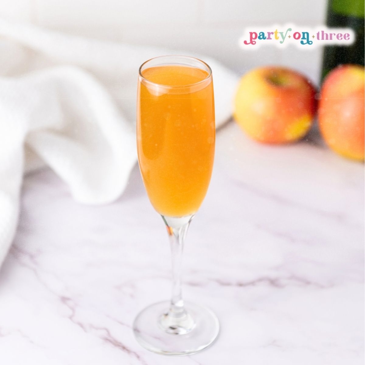 Apple Cider Mimosa in a champagne flute on a marble counter with apples and a bottle in the background