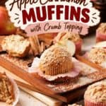 Apple cinnamon muffins with crumb topping in pink liners, arranged on a wooden board with cinnamon sticks and apple slices