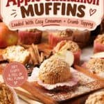 Apple cinnamon muffins with crumb topping on a wooden board, surrounded by cinnamon sticks and apple slices