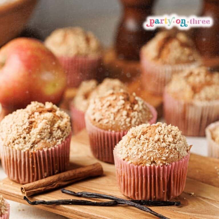 Apple cinnamon muffins with crumble topping in pink liners, with cinnamon sticks and vanilla beans.