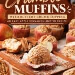 Apple cinnamon muffins with buttery crumble topping on a wooden board, surrounded by apples and cinnamon sticks