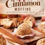 Apple cinnamon muffins with crumb topping on a wood board, surrounded by cinnamon sticks and apple slices