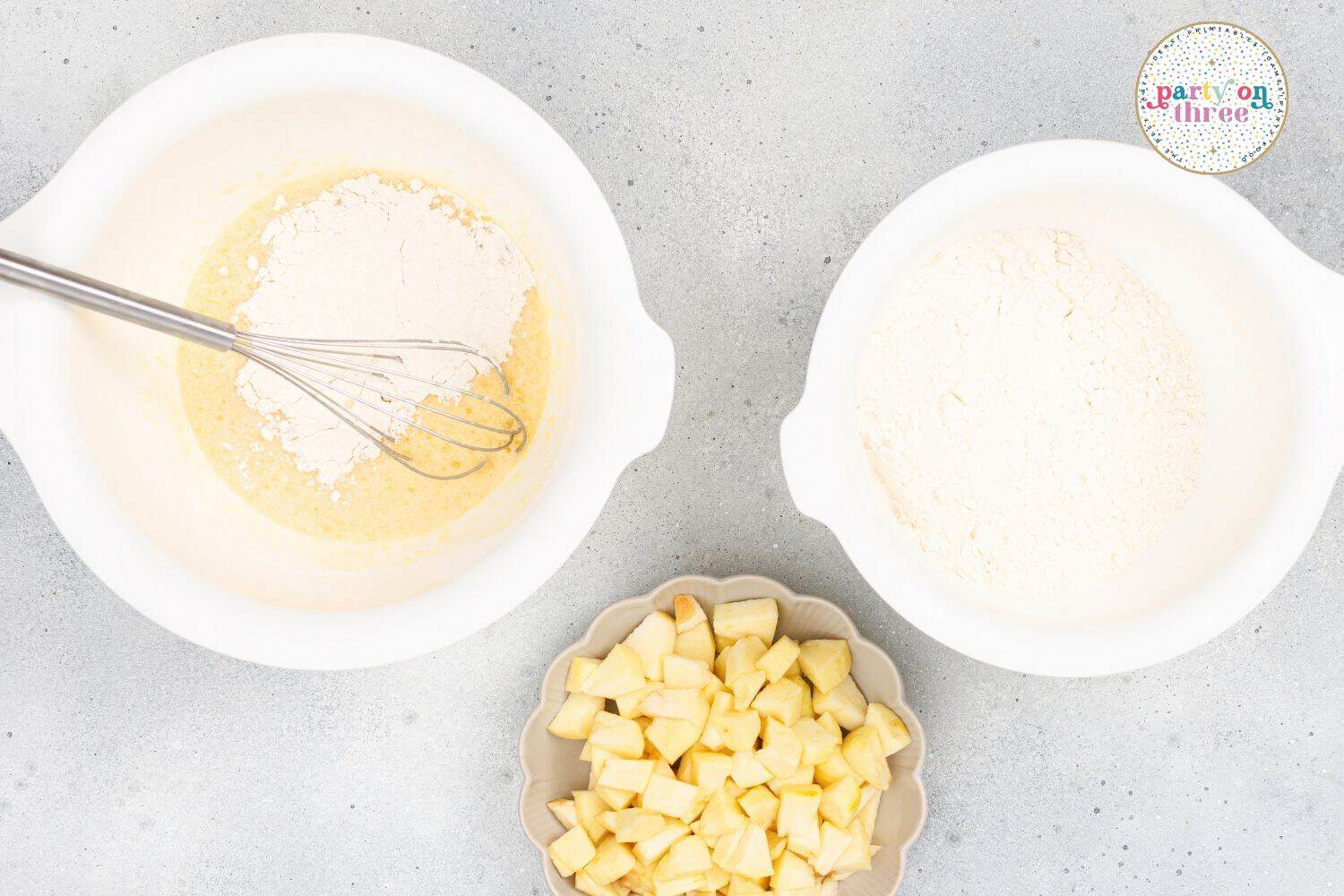 Whisking flour into wet batter with flour mixture and diced apples in bowls nearby