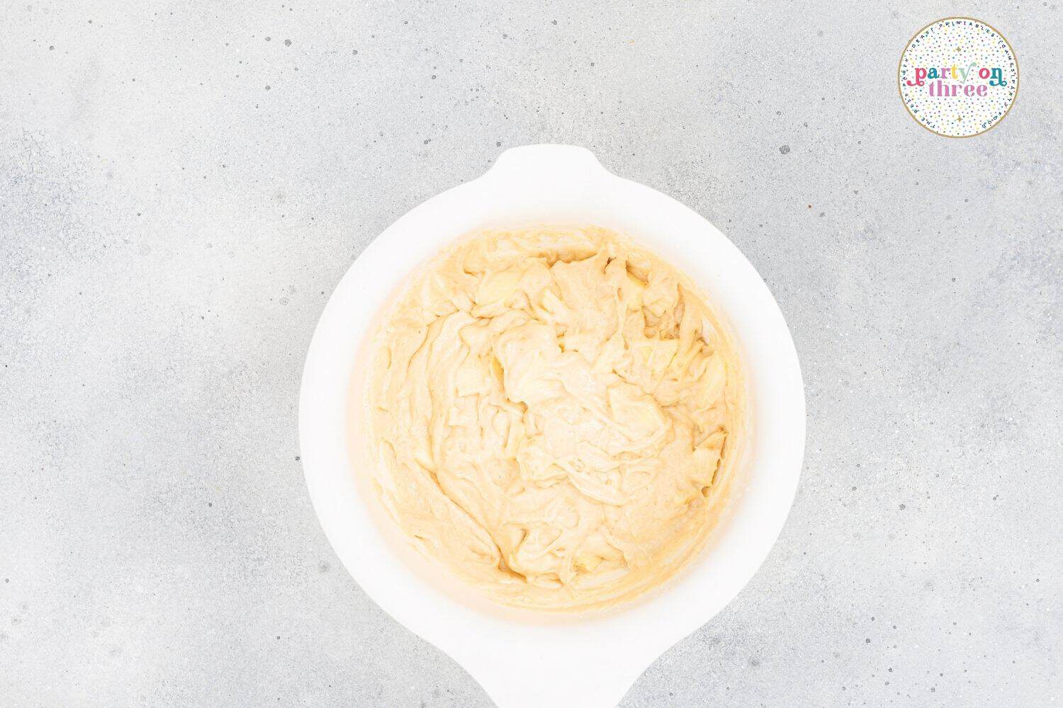 Freshly mixed apple cinnamon muffin batter in a white bowl, with a few small lumps visible