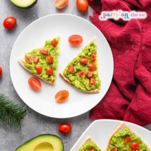 Christmas appetizer triangles of avocado pita topped with diced tomatoes, served on white plates with cherry tomatoes