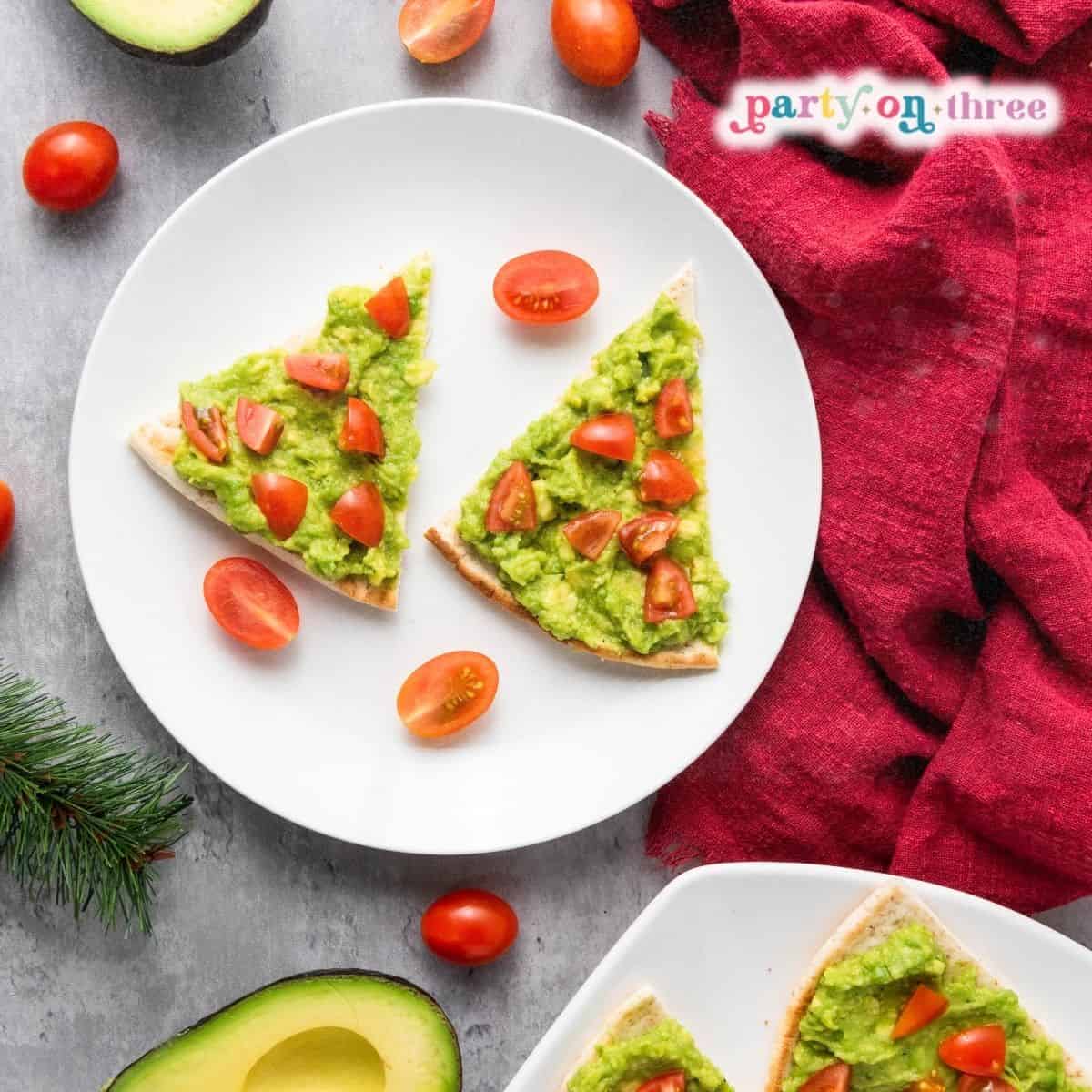 Christmas appetizer triangles of avocado pita topped with diced tomatoes, served on white plates with cherry tomatoes