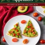 Triangle pita slices topped with mashed avocado and tomatoes, styled as Christmas trees on a white plate.