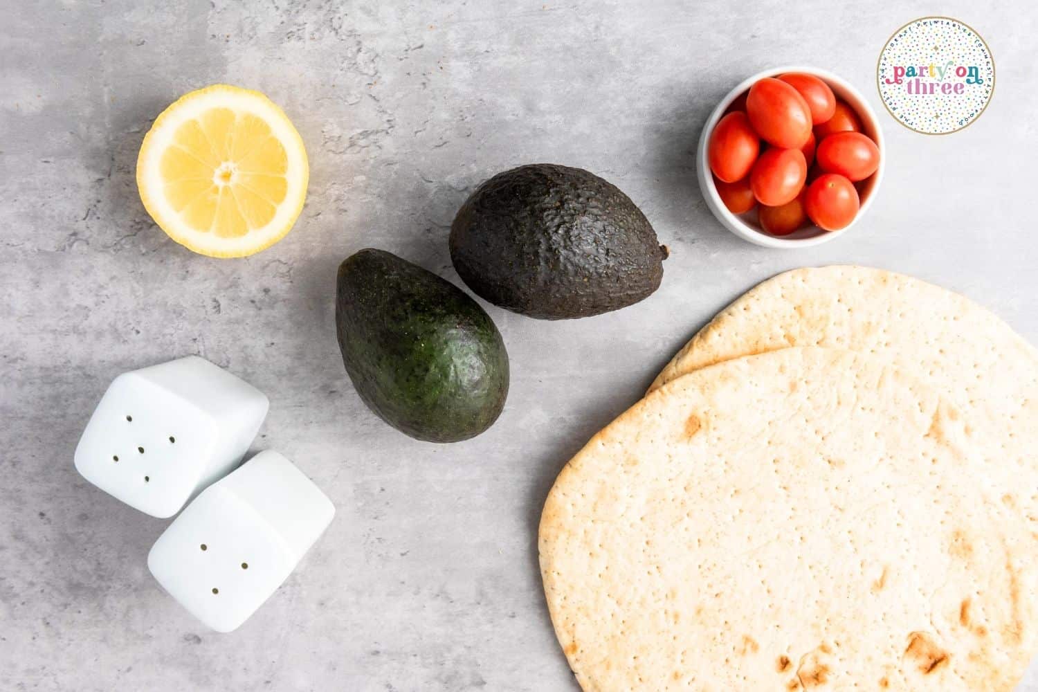 Ingredients for Christmas appetizer: avocados, pita bread, cherry tomatoes, lemon half, and salt and pepper shakers