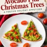 Two pita triangles topped with mashed avocado and diced tomatoes shaped like Christmas trees on a white plate