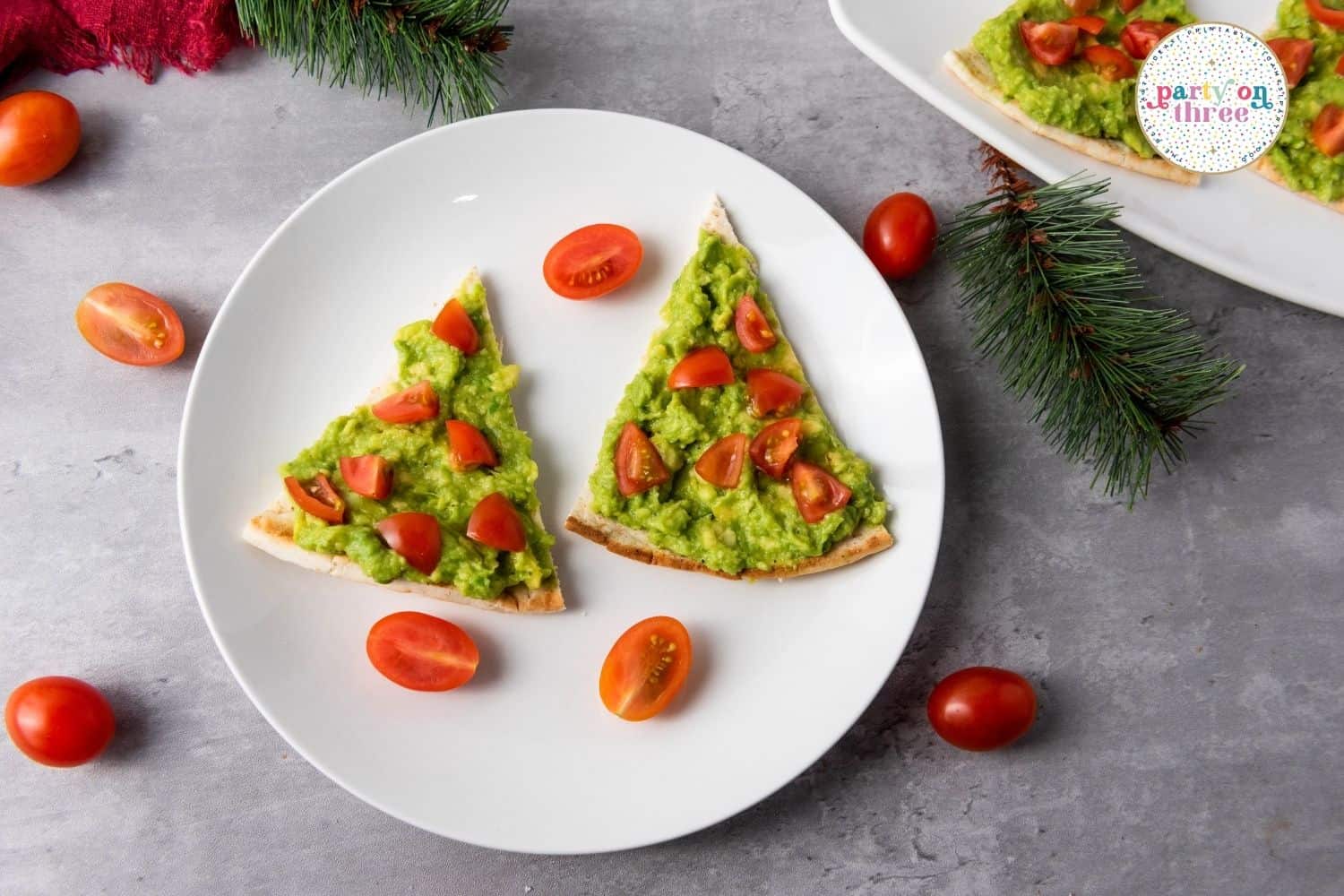 Triangle pita slices topped with mashed avocado and diced cherry tomatoes, plated with whole tomatoes around
