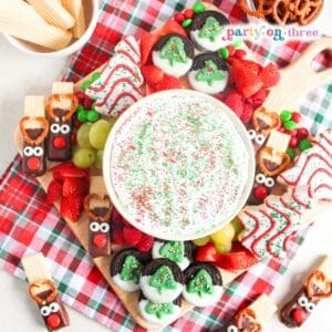 Christmas charcuterie board with marshmallow fruit dip, reindeer pretzels, dipped Oreos, fruit, and candy