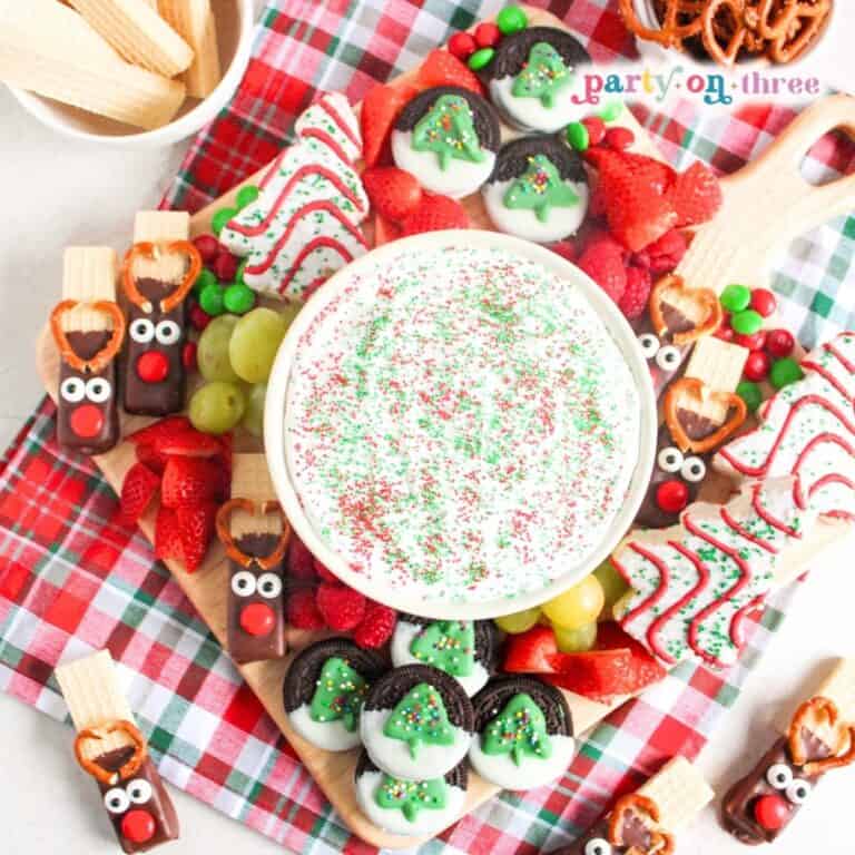Christmas charcuterie board with marshmallow fruit dip, reindeer pretzels, dipped Oreos, fruit, and candy