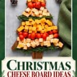Christmas tree shaped cheese board with cubed cheese, cherry tomatoes, and rosemary sprigs on a wooden tray