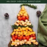 Christmas cheese board shaped like a tree with cheddar, cheese cubes, tomatoes, and rosemary on a wooden board