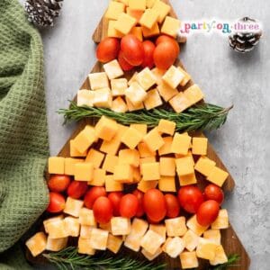 Christmas tree shaped cheese board with cheddar cubes, cherry tomatoes, and rosemary sprigs on a wooden board