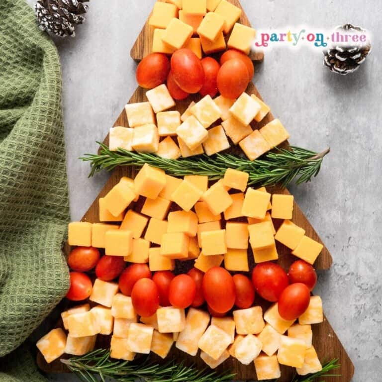 Christmas tree shaped cheese board with cheddar cubes, cherry tomatoes, and rosemary sprigs on a wooden board
