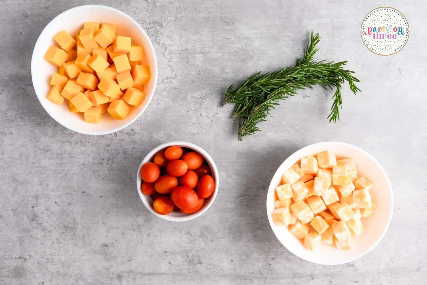 Ingredients for Christmas cheese board: cubed cheddar and white cheese, cherry tomatoes, and fresh rosemary sprigs