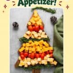 Christmas tree shaped cheese board with cheddar cubes, cherry tomatoes, and rosemary sprigs on a wooden board