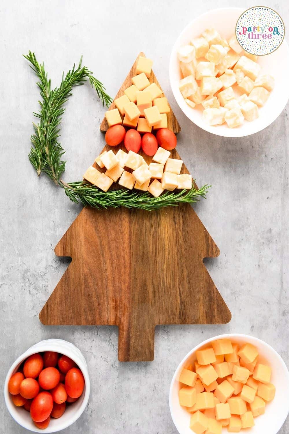 Arranging cheese cubes and cherry tomatoes with rosemary sprigs on a tree-shaped board to form a Christmas tree