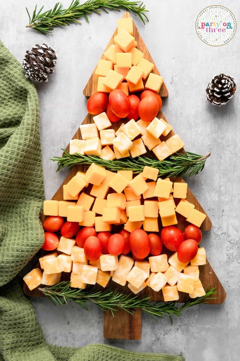 Tree-shaped board with layered cheese cubes, cherry tomatoes, and rosemary sprigs forming a Christmas tree pattern